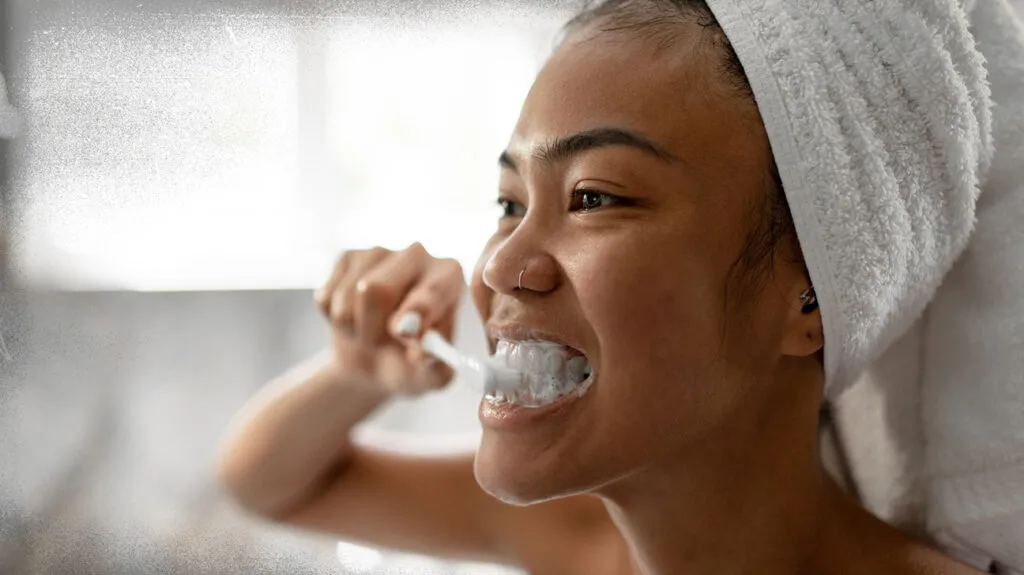 Kvinne som pusser tenner, noe som er viktig før tannbleking