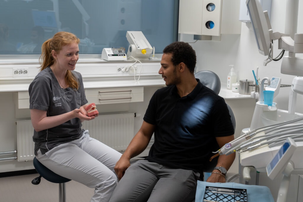 "Tannpleier viser en tannmodell til en pasient under en konsultasjon i et moderne tannlegekontor med profesjonelt utstyr."